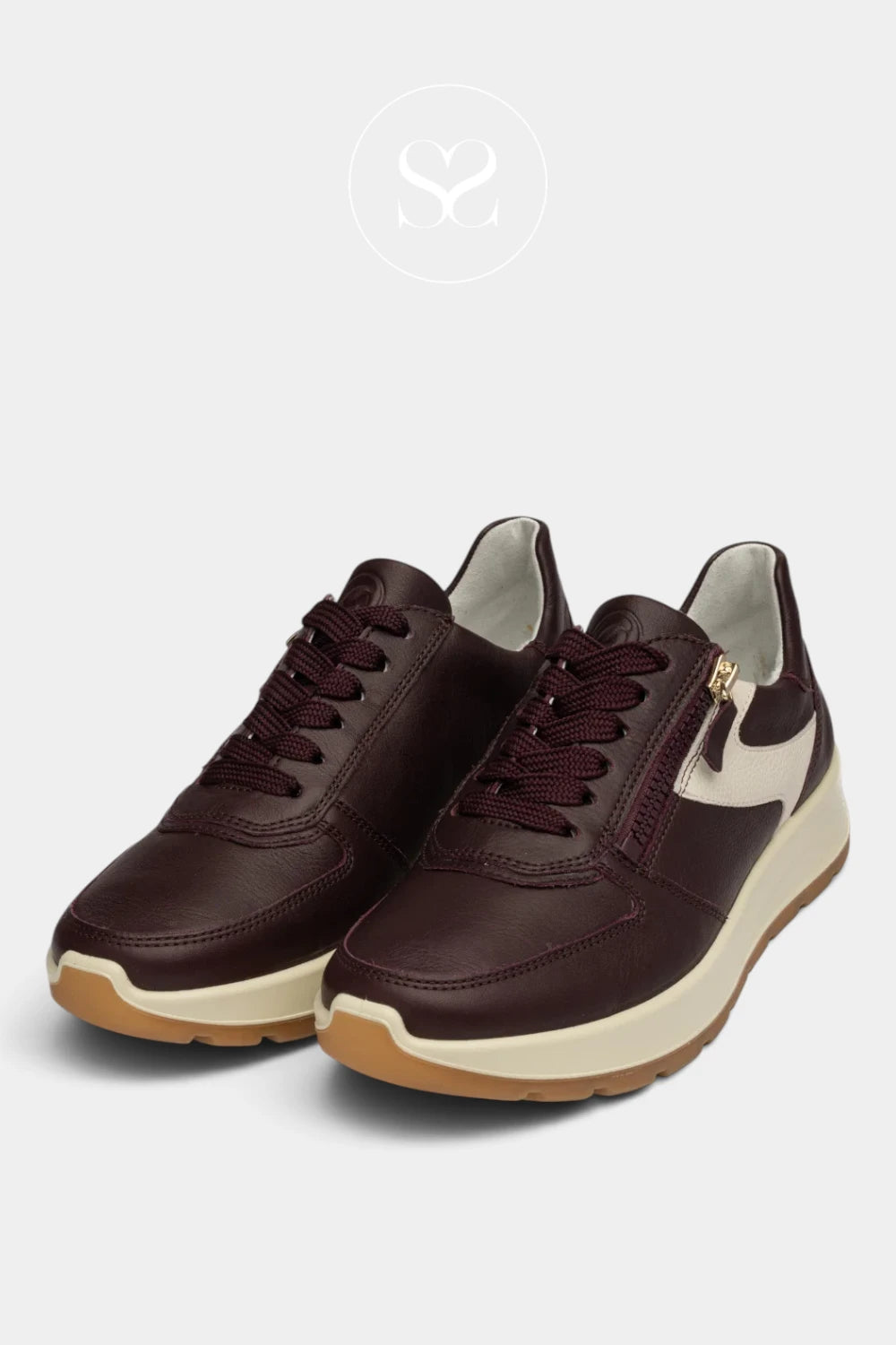 A pair of low-top sneakers in dark burgundy leather with cream side panels, cream midsoles, and gum outsoles, shown on a light gray background with a faint brand logo above.