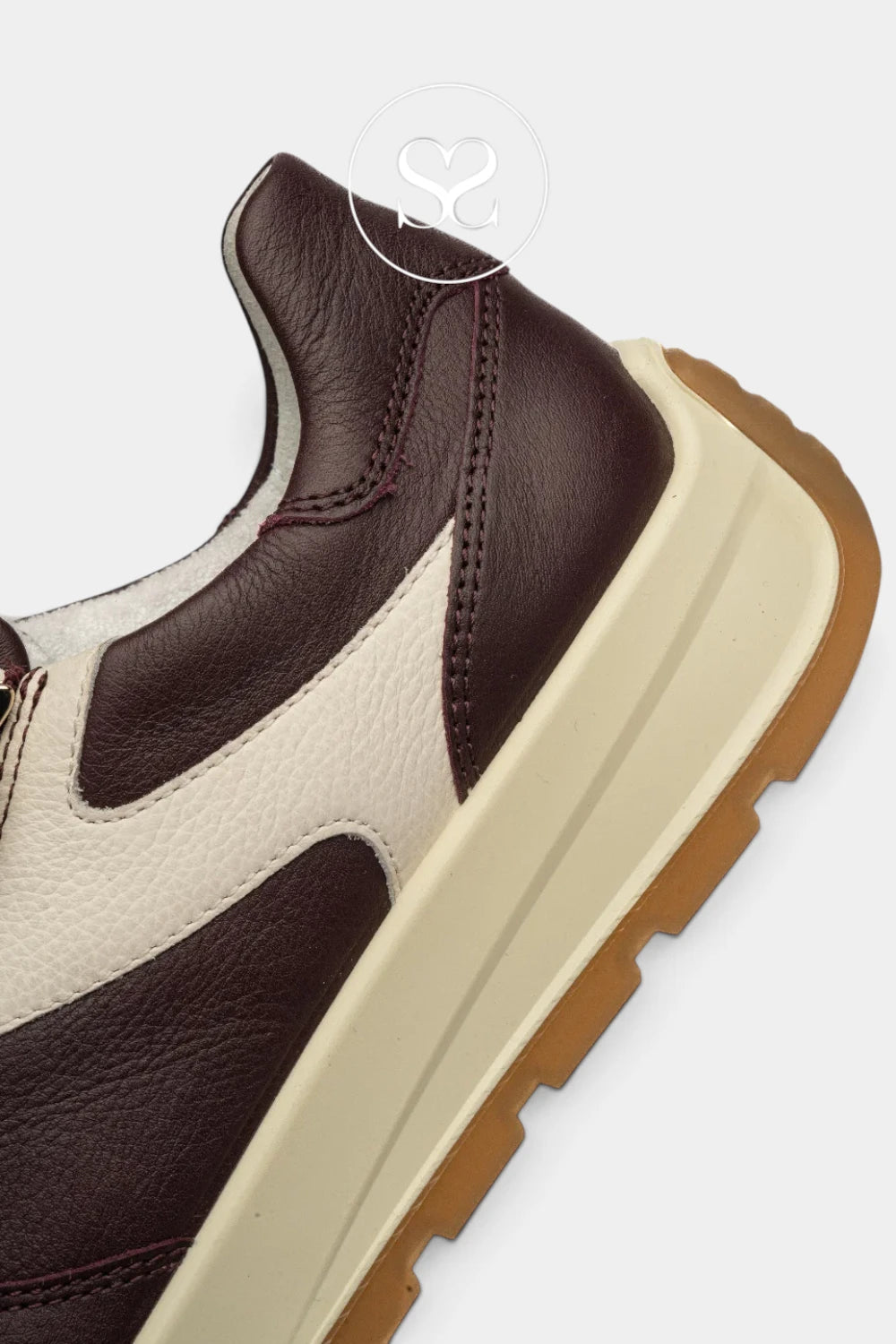 Close-up of a low-top sneaker showing the heel and side panel, with dark brown leather, cream leather overlays, a thick cream midsole, and a gum brown outsole on a light gray background.