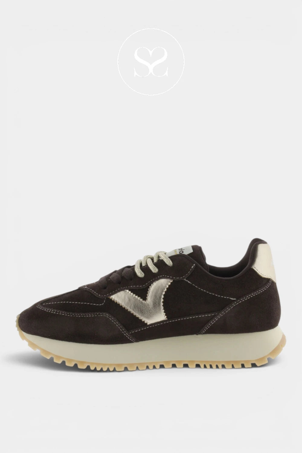 A dark brown suede sneaker with a metallic silver chevron logo on the side, cream laces, and a cream midsole with a gum outsole, shown against a light gray background.