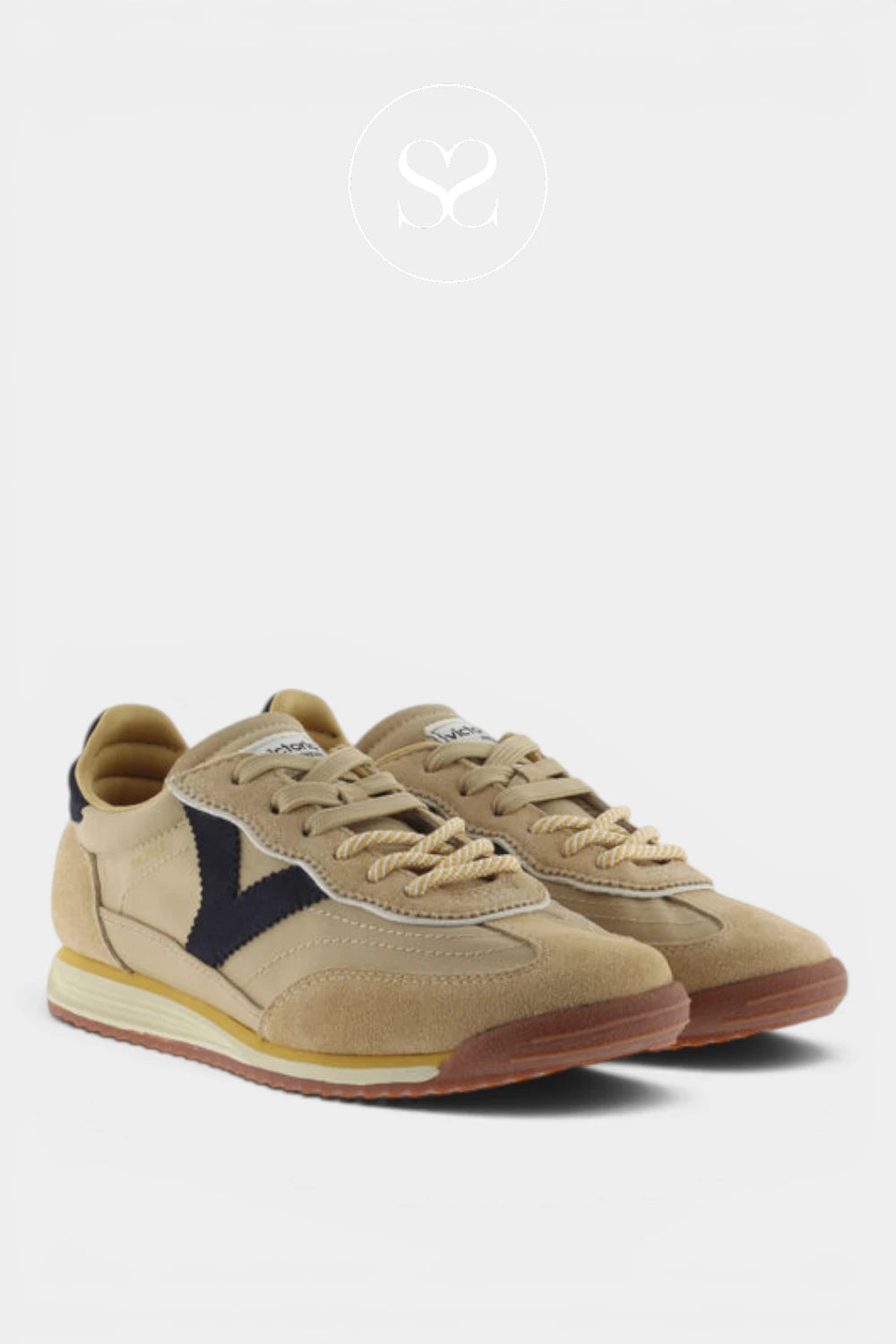 A pair of beige suede sneakers with navy blue side stripes, beige laces, and a brown gum sole, displayed on a light gray background.