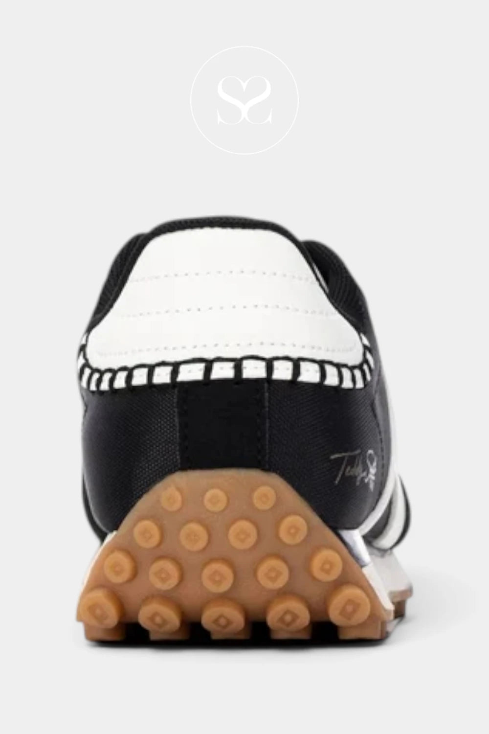A close-up rear view of a black and white sneaker with a distinctive brown gum sole featuring circular tread patterns, set against a light gray background.
