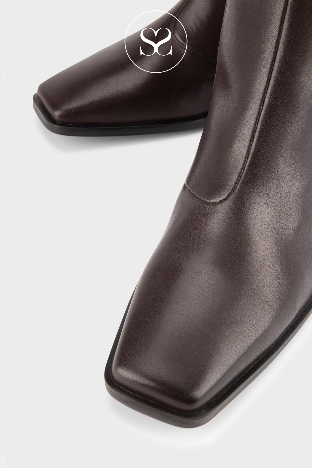 A close-up of a dark brown leather boot with a square toe, featuring a side seam and a circular Sheneil Shoes logo overlay on the upper.