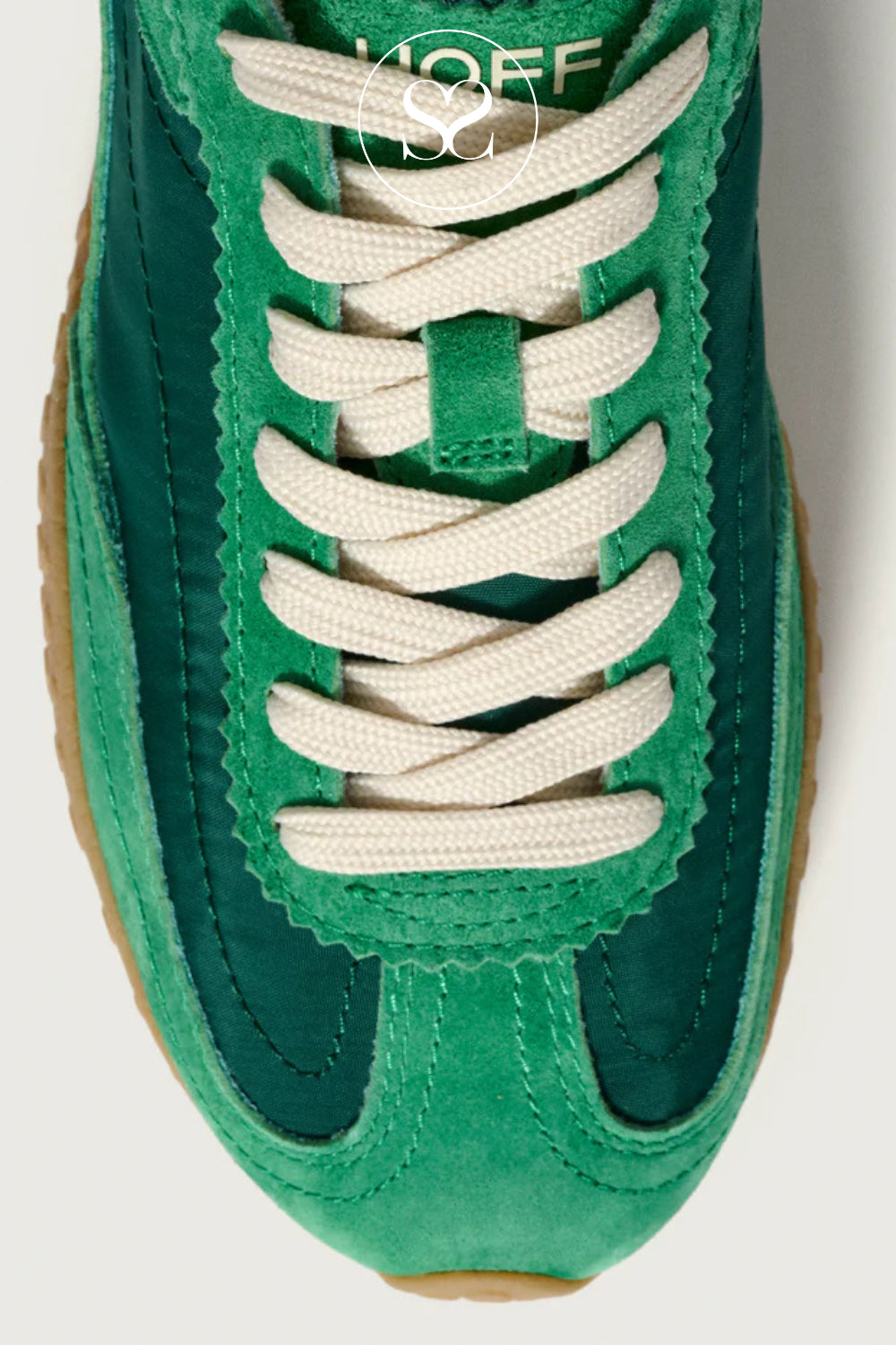 Green sneaker with white laces on a light grey background