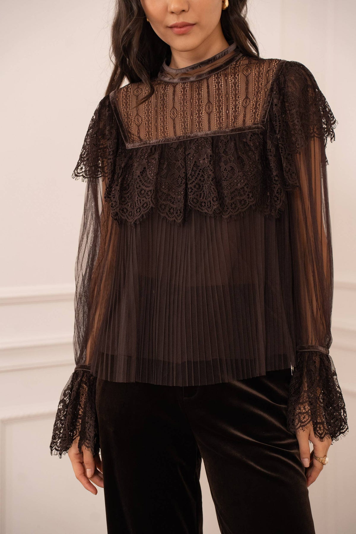 Woman wearing a dark brown lace-trimmed blouse against a white background