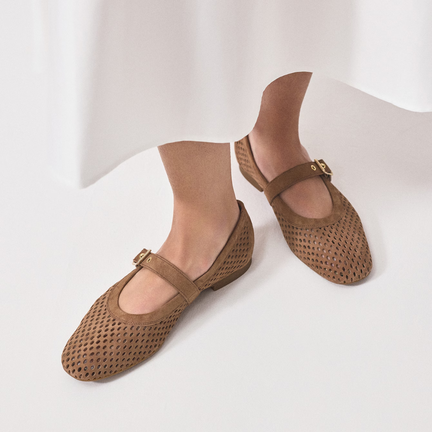 Brown mesh ballet flats worn by a person on a white background