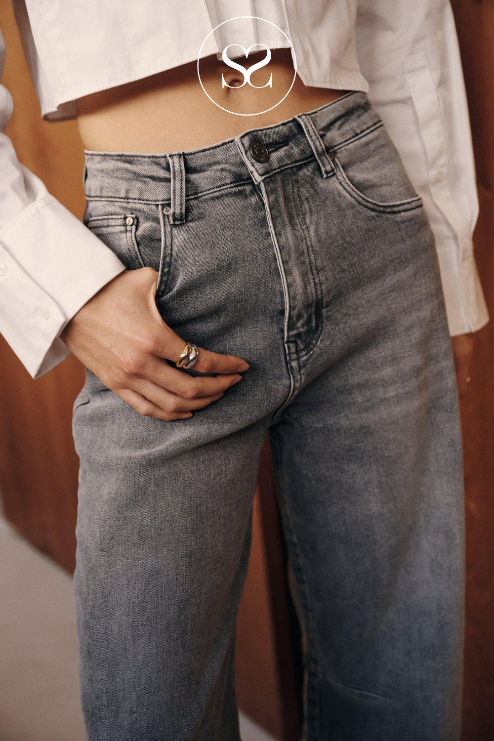 Close-up of a person wearing high-waisted gray washed denim jeans with a white cropped top.