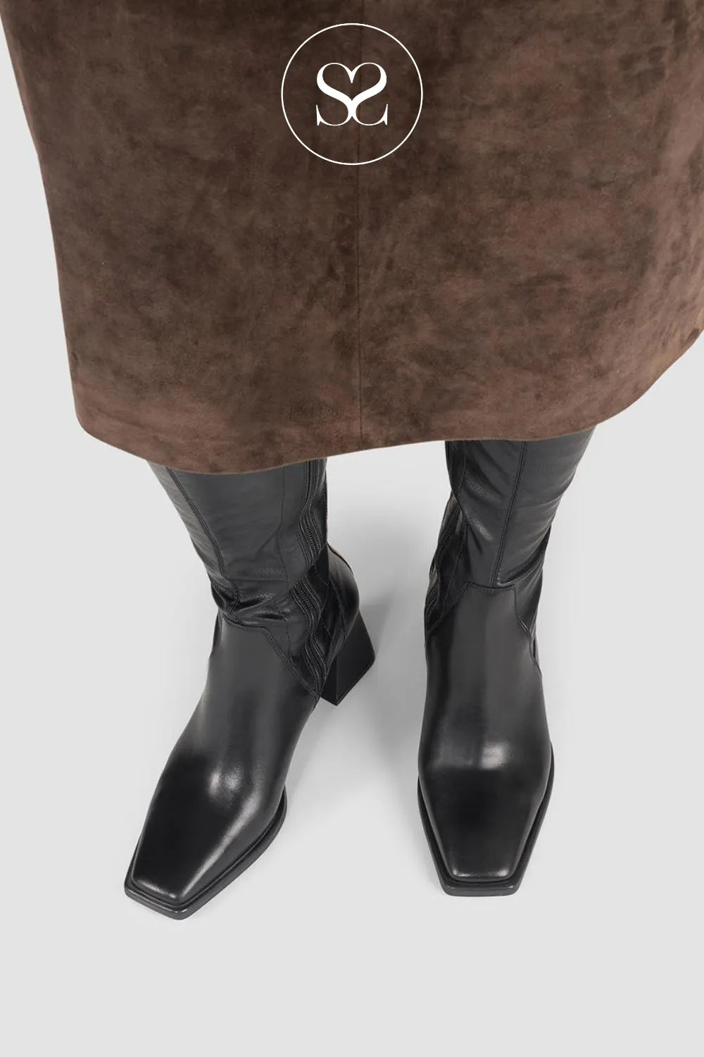 Black boots worn with a brown coat on a light gray background