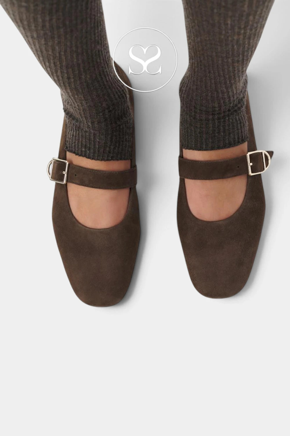 A top-down view of a person wearing dark brown suede Mary Jane shoes with square toes and gold-tone buckle straps, paired with ribbed dark brown socks on a light gray background.