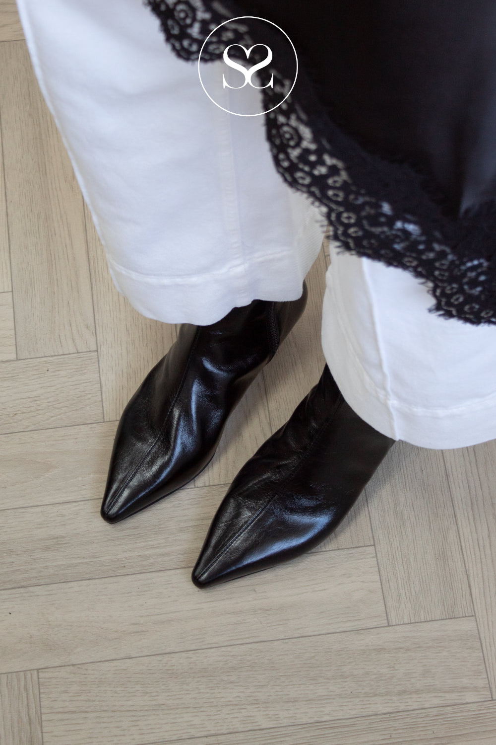 A close-up of a person wearing black pointed-toe leather ankle boots from Angel Alarcon