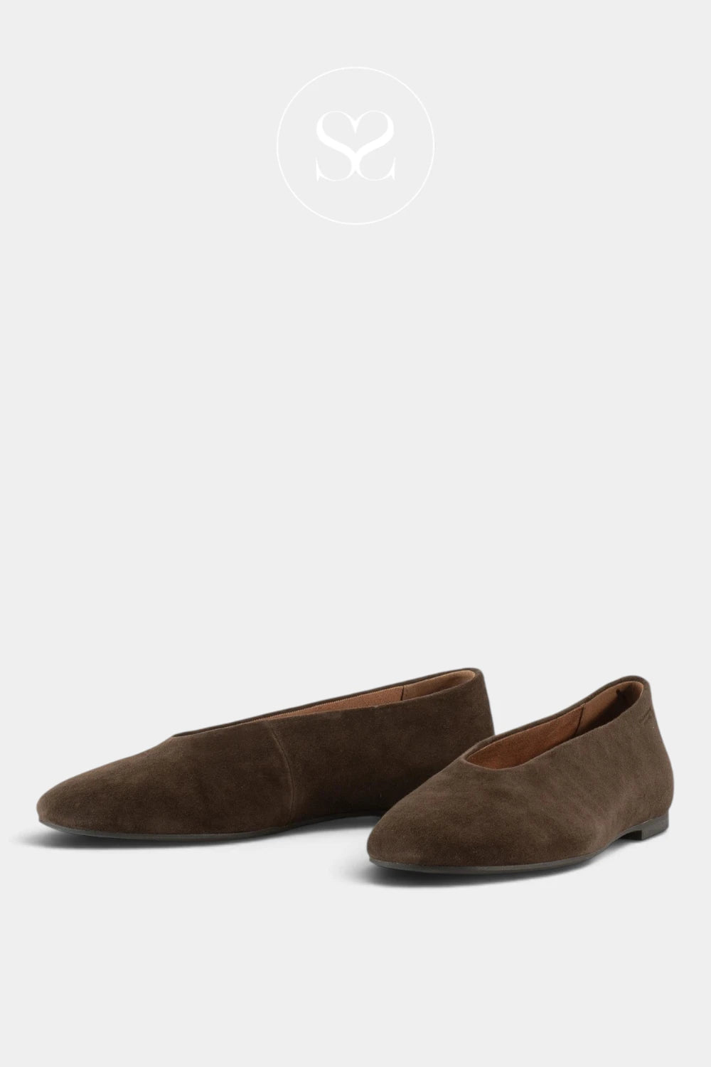 A pair of dark brown suede ballet flats with pointed toes, displayed on a light gray background with a faint circular logo at the top.
