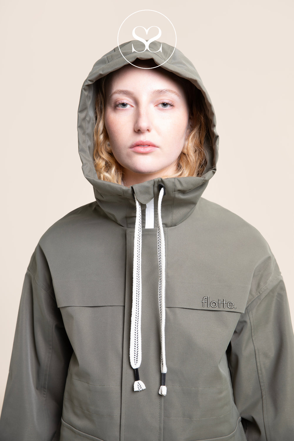 A model wearing an olive green hooded jacket with white drawstrings and a small embroidered 'flotte' logo on the chest, set against a solid beige background.