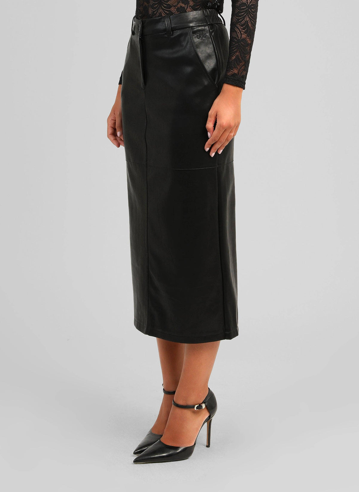 A model wearing a black faux-leather midi skirt with a matching black belt, paired with black pointed-toe heels, shown against a light gray studio background.