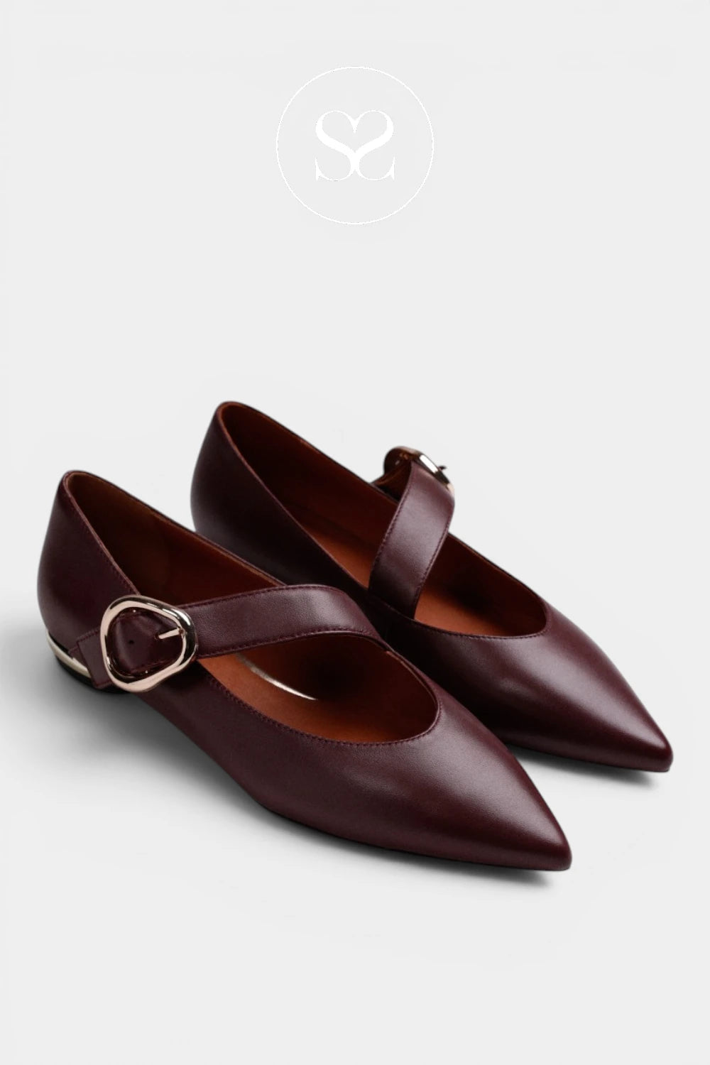 A pair of dark burgundy leather Mary Jane flats with pointed toes and gold-tone buckle straps, displayed on a light gray background.