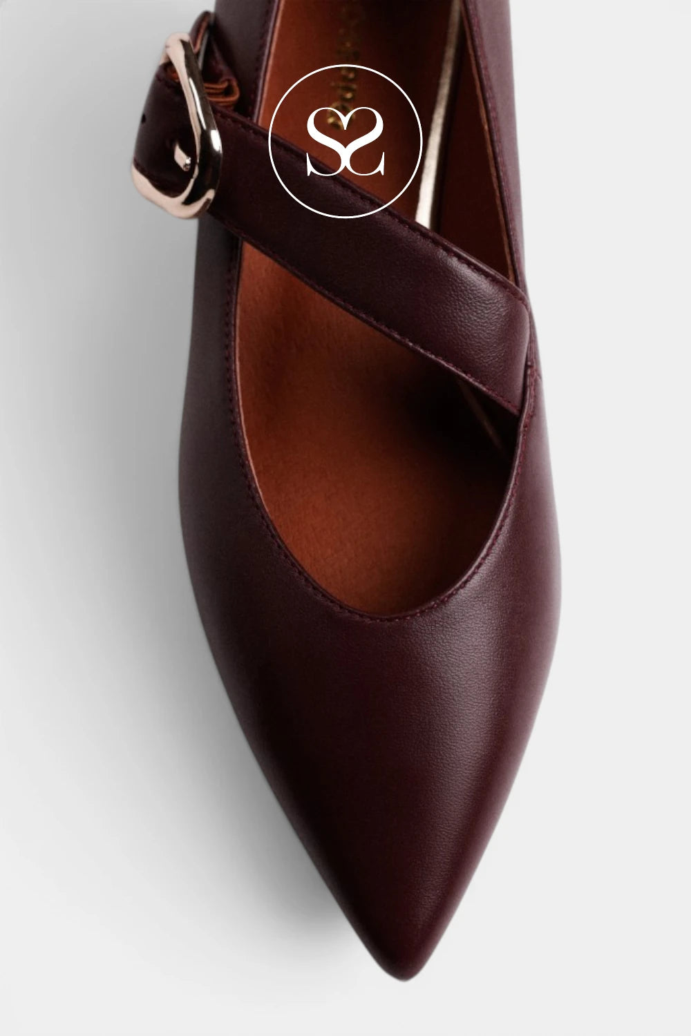A close-up of a dark burgundy pointed-toe pump with a decorative strap and gold-tone buckle, shown on a light gray background with a circular 'S2' logo overlay.