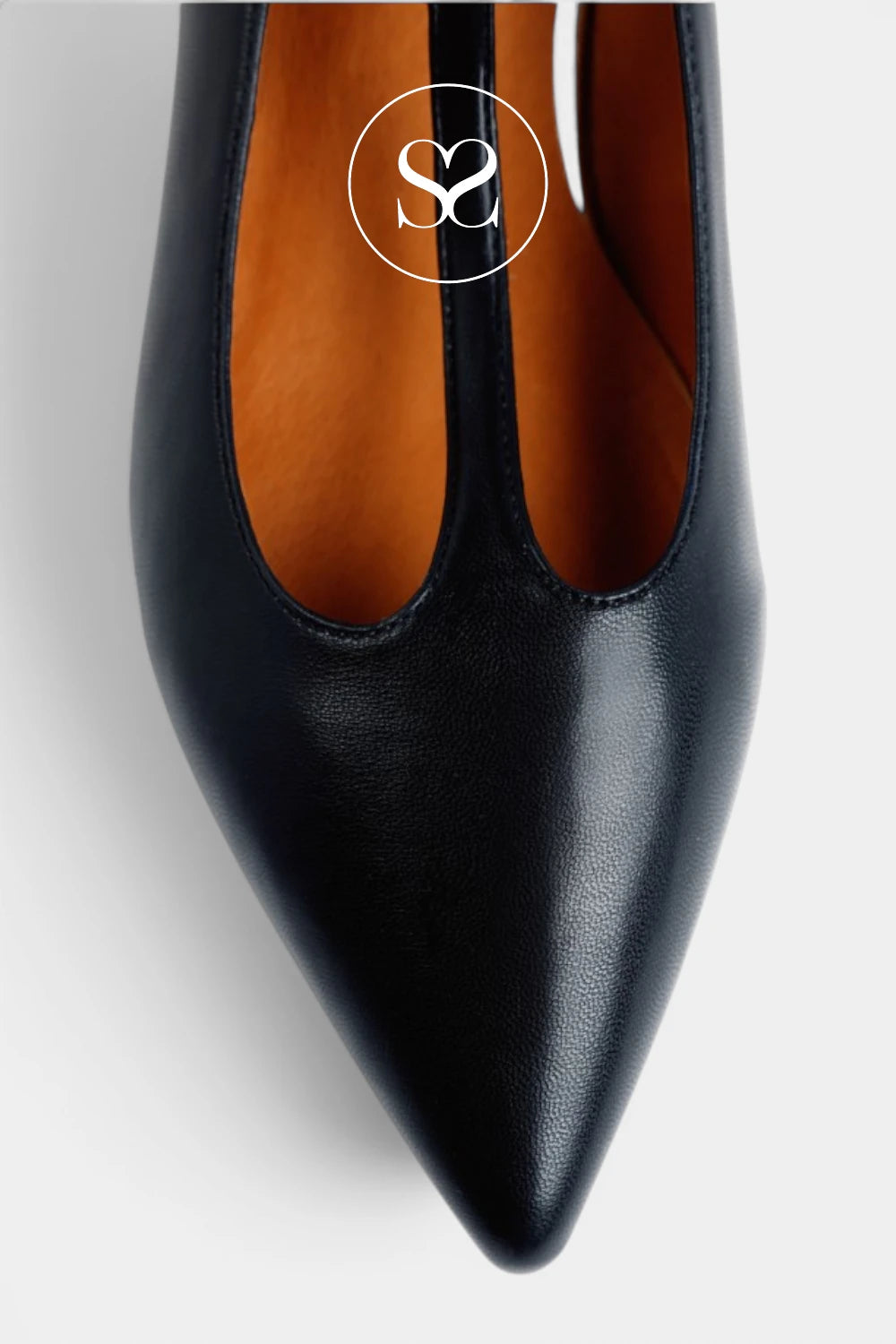 A close-up top-down view of a black pointed-toe pump with a split V-cut vamp, showing a warm tan interior and a white circular 'S2' logo overlay near the top center.