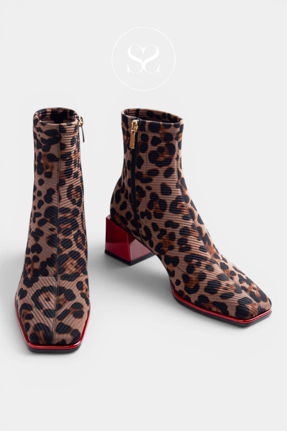 A pair of ankle boots with a brown and black leopard print pattern, featuring a textured ribbed fabric, square toes, and chunky red block heels, shown against a light gray background.