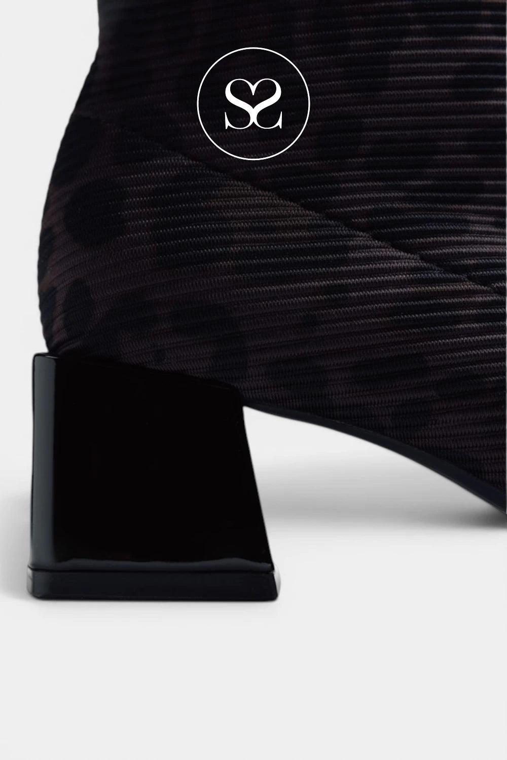 Close-up of a black textured ankle boot with a glossy block heel, featuring a circular white logo overlay on the side.