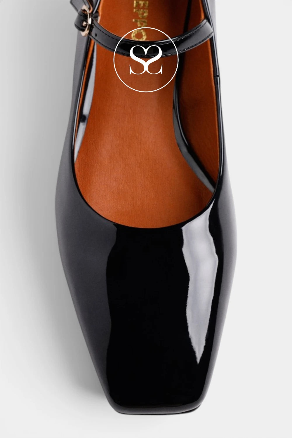 A close-up of a glossy black patent leather Mary Jane shoe with a square toe and a brown insole, featuring a circular logo overlay on the upper.