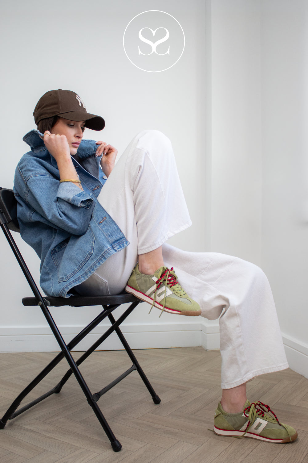 Person sitting on a chair wearing a denim jacket, white pants, and green sneakers with double lace detail from Back 70