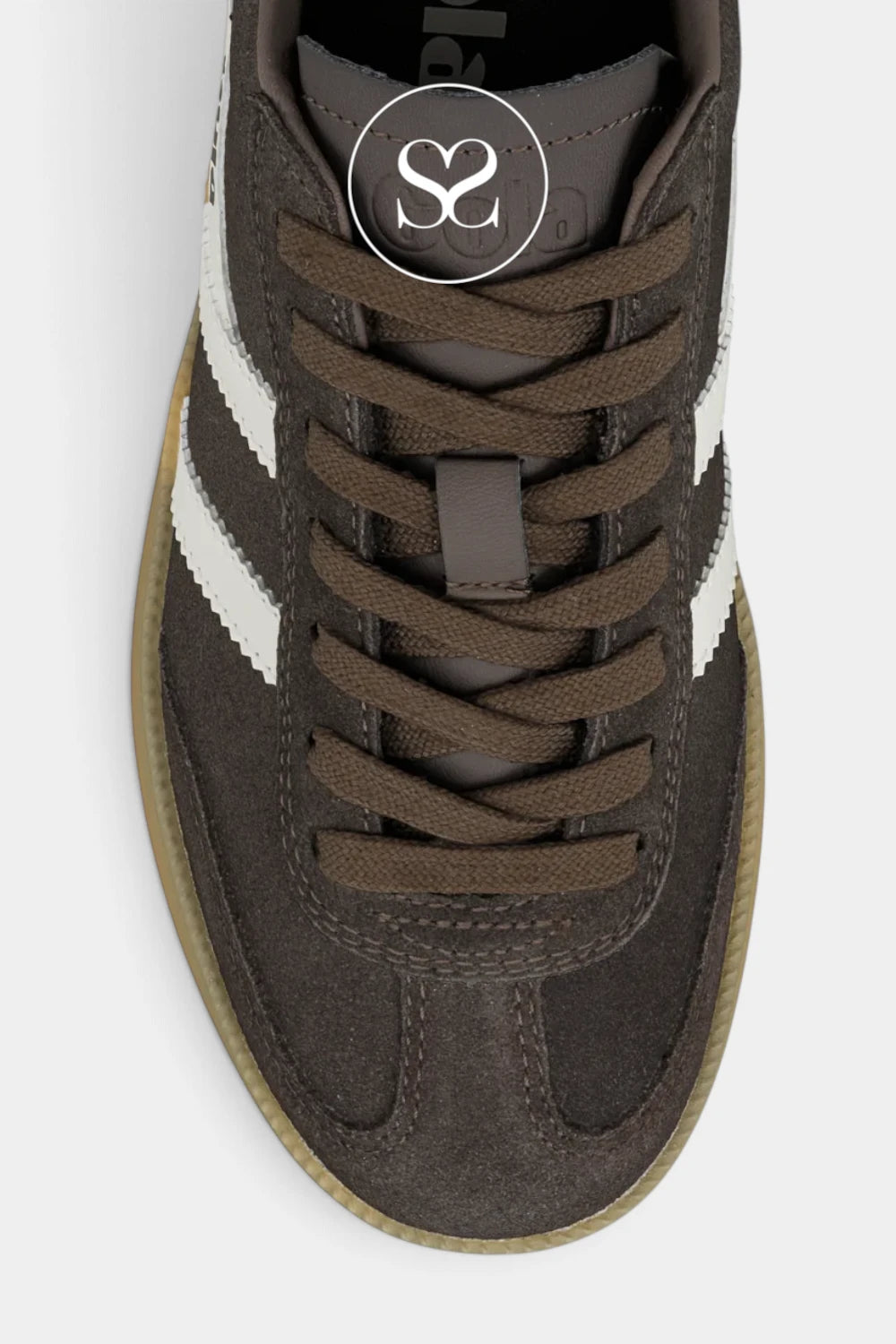 A top-down close-up of a dark brown suede sneaker with white side stripes, brown laces, and a tan rubber sole, featuring a circular logo overlay on the tongue.