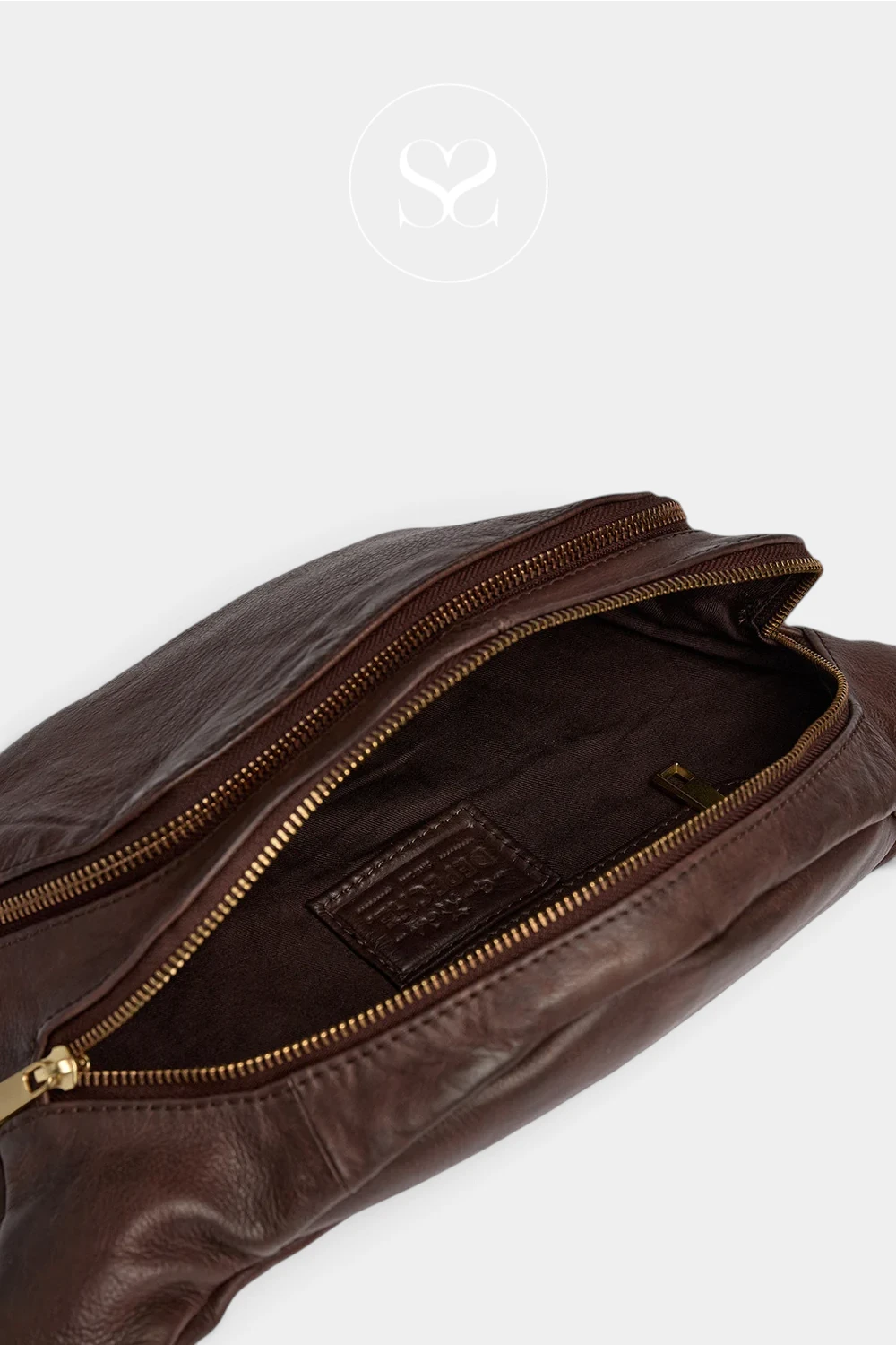 Close-up of a dark brown leather bag with an open gold zipper, showing the interior lining and a small embossed brand patch inside, on a light gray background.
