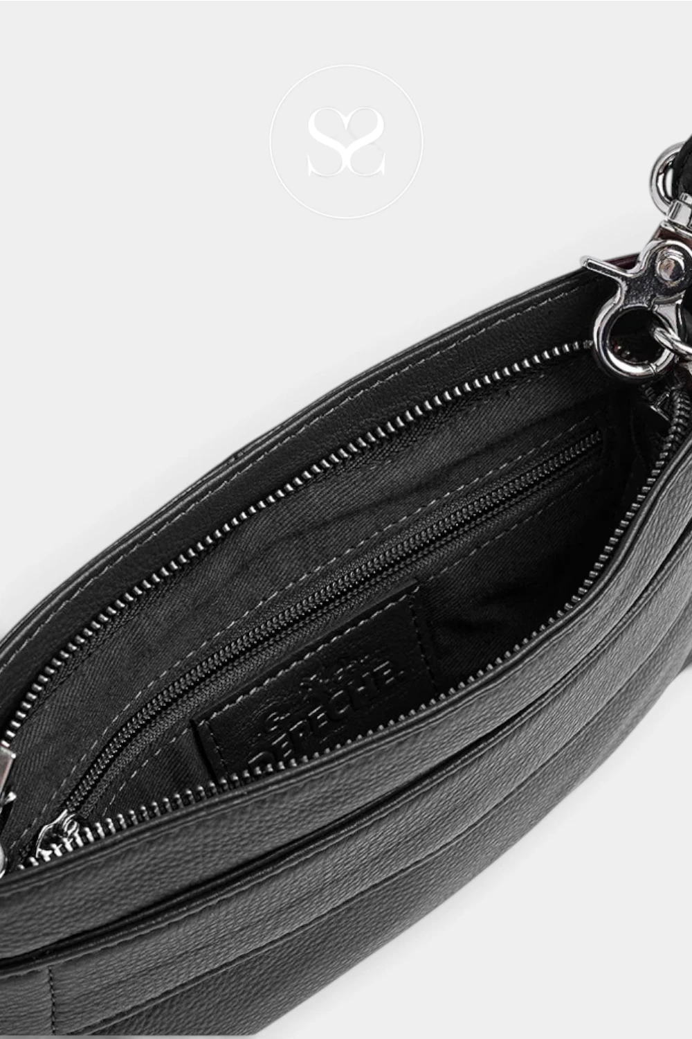 Close-up of a black leather handbag interior showing a zippered compartment, black fabric lining, and a silver-tone metal clasp on a light gray background.