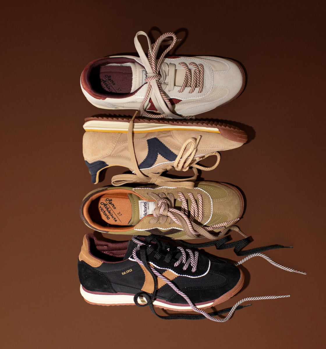 Four retro-style women's trainers arranged vertically on a solid brown background. The shoes feature chunky platform soles and are shown in cream, beige, olive green, and black colorways, each with their laces tied in a neat bow.