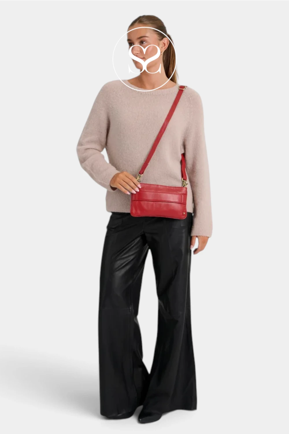 A woman modeling a light beige knit sweater, black wide-leg pants, and a red crossbody bag with gold hardware against a light gray background.