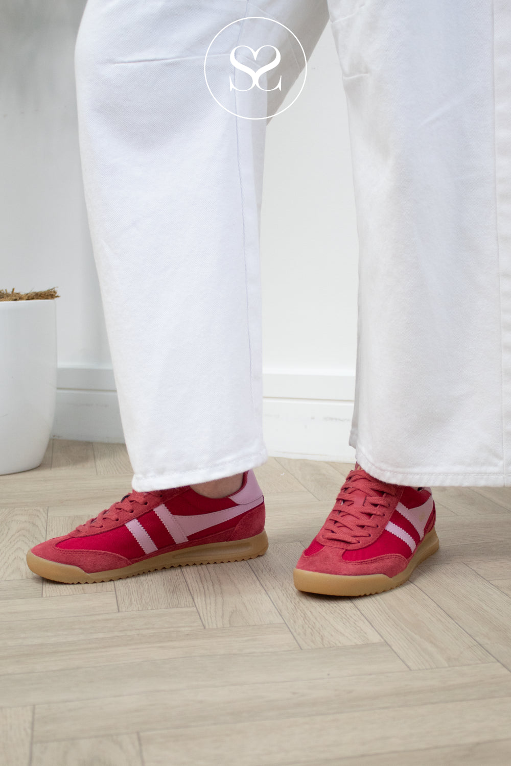 Red sneakers with pink accents from Gola worn with white pants on a light wooden floor.