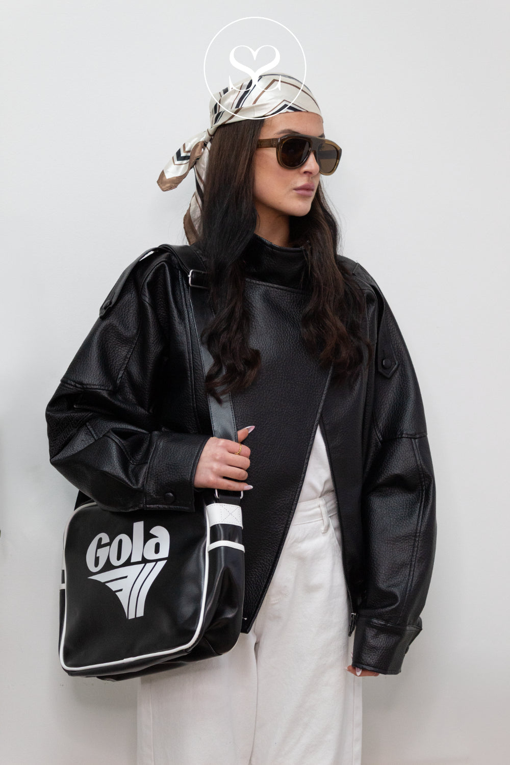 Person wearing a black leather jacket and holding a black Gola Redford bag against a white background