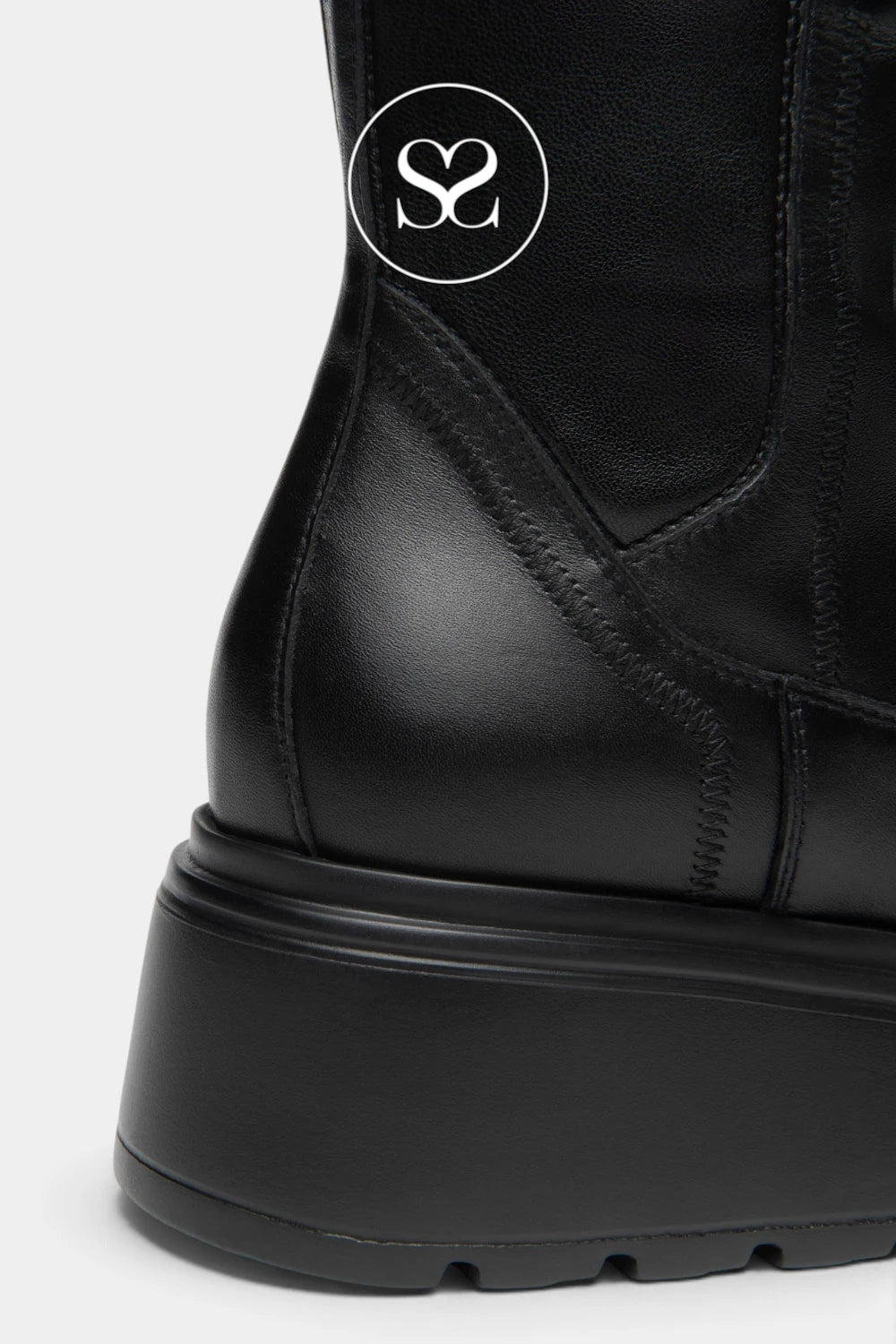 Close-up of a black leather ankle boot with a chunky black sole, featuring a circular white logo on the side.