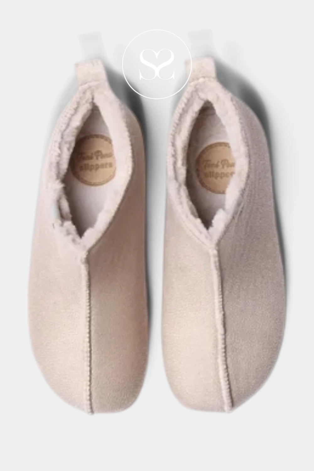 A pair of light beige slip-on slippers with soft cream fleece lining, shown from a top-down view on a light gray background. A circular logo watermark is visible at the top center.
