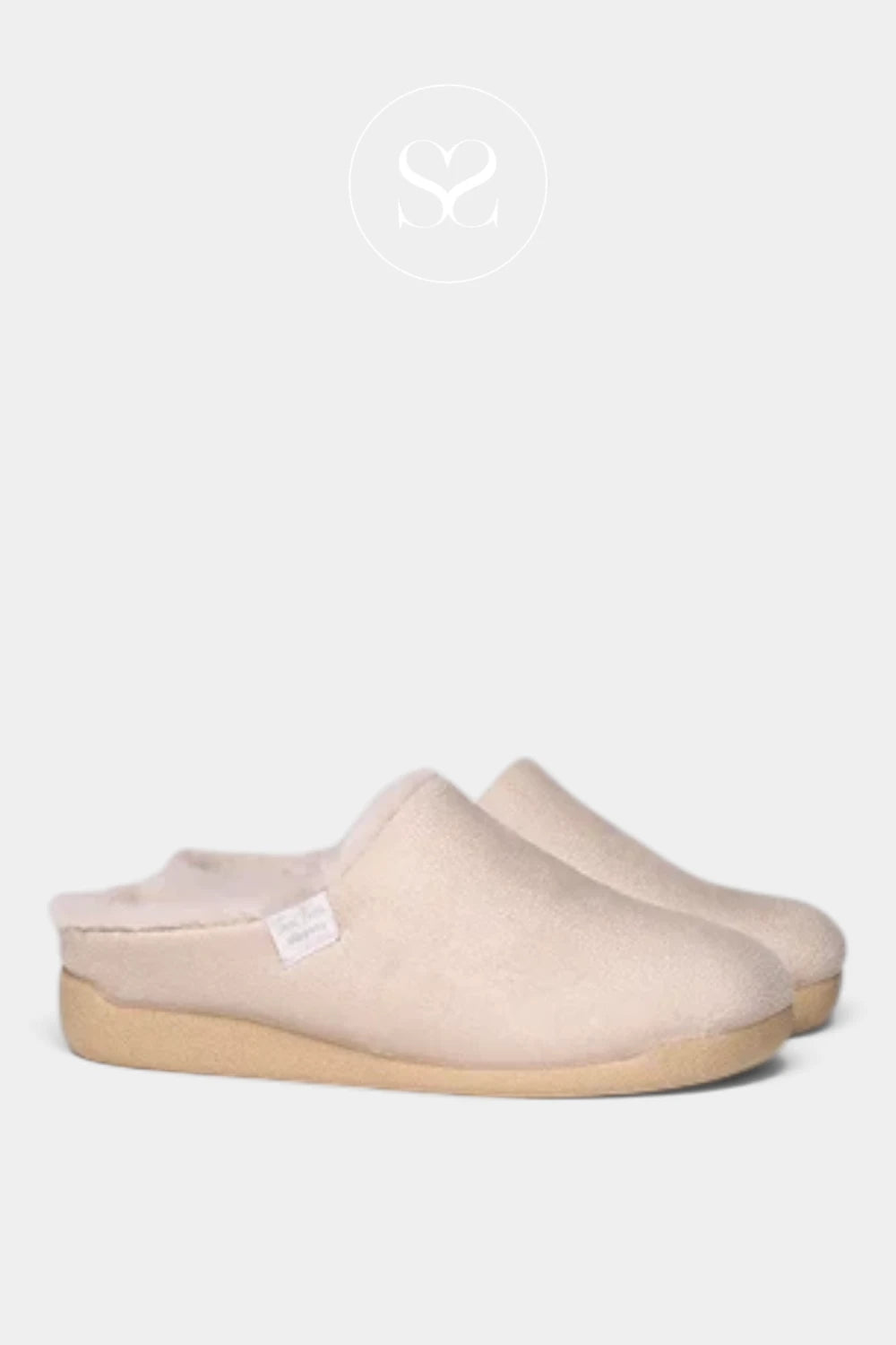 A pair of slip-on mule slippers in a soft blush pink fabric with a natural tan sole, shown against a light gray background with a faint brand logo at the top.