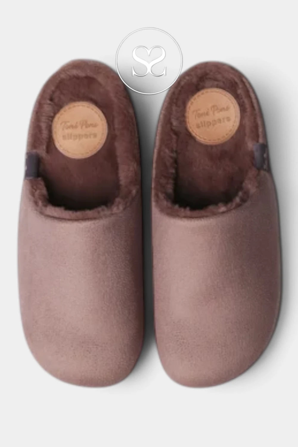 A pair of Taupe suede slipper shoes with soft brown faux fur lining, shown from a top-down view on a light gray background. A circular logo watermark is visible at the top center.