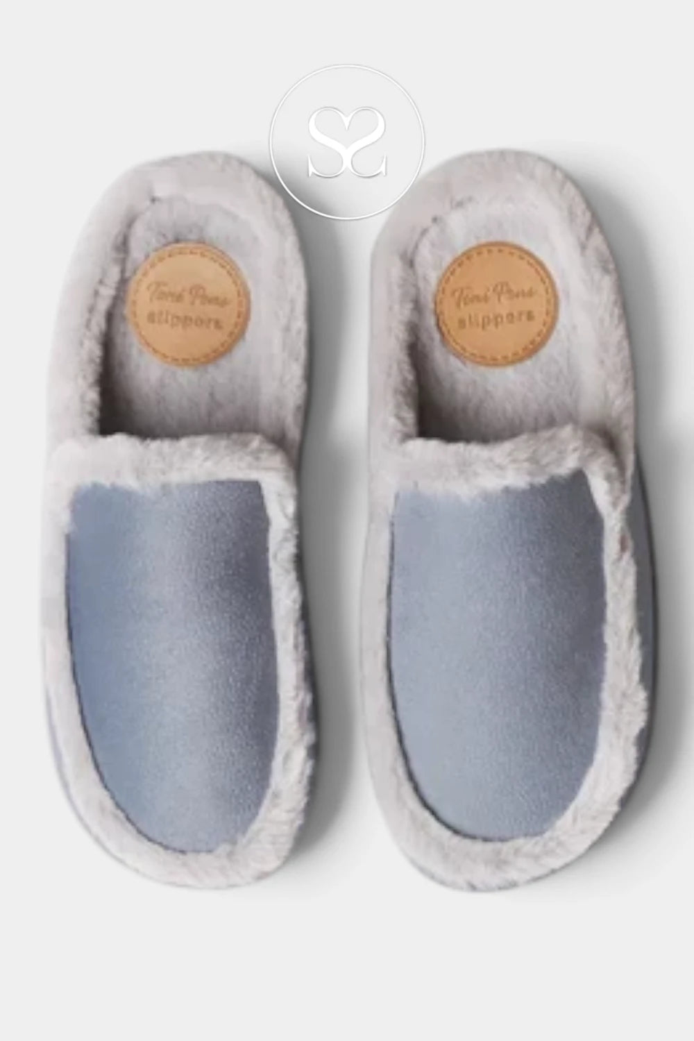 A pair of slip-on slippers with a light blue velvet-like upper and fluffy light gray trim, shown from a top-down view on a light gray background. A circular logo watermark is visible at the top center, and a small tan brand patch is visible on the insole of each slipper.