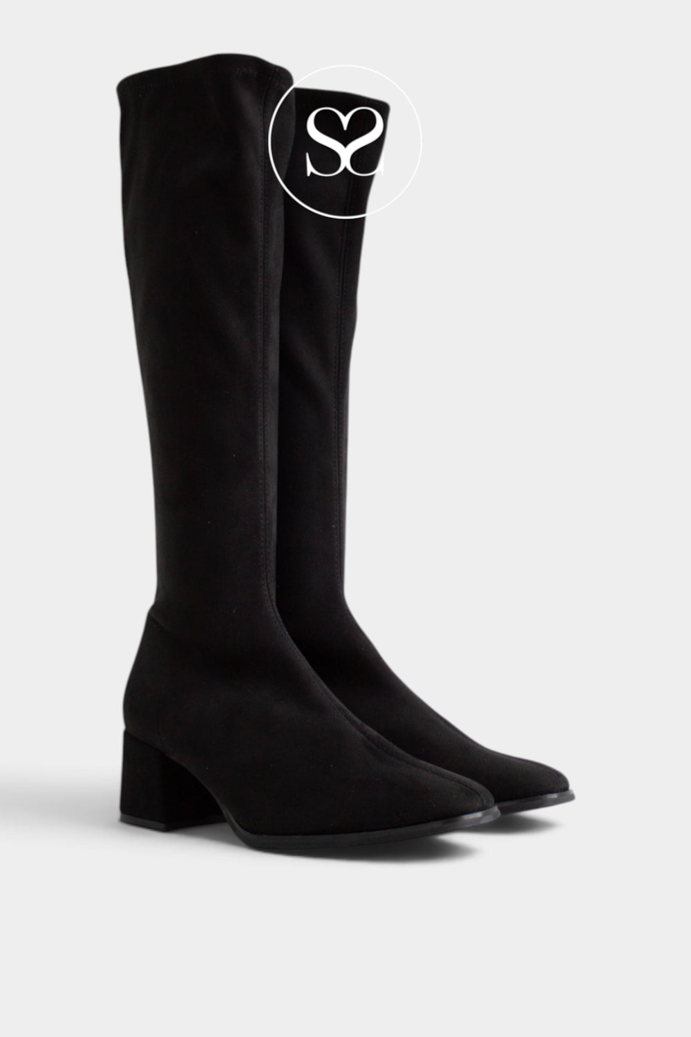 A pair of Miss Elastic black suede knee-high boots with a block heel and almond toe, shown on a light gray background with a white circular logo overlay.