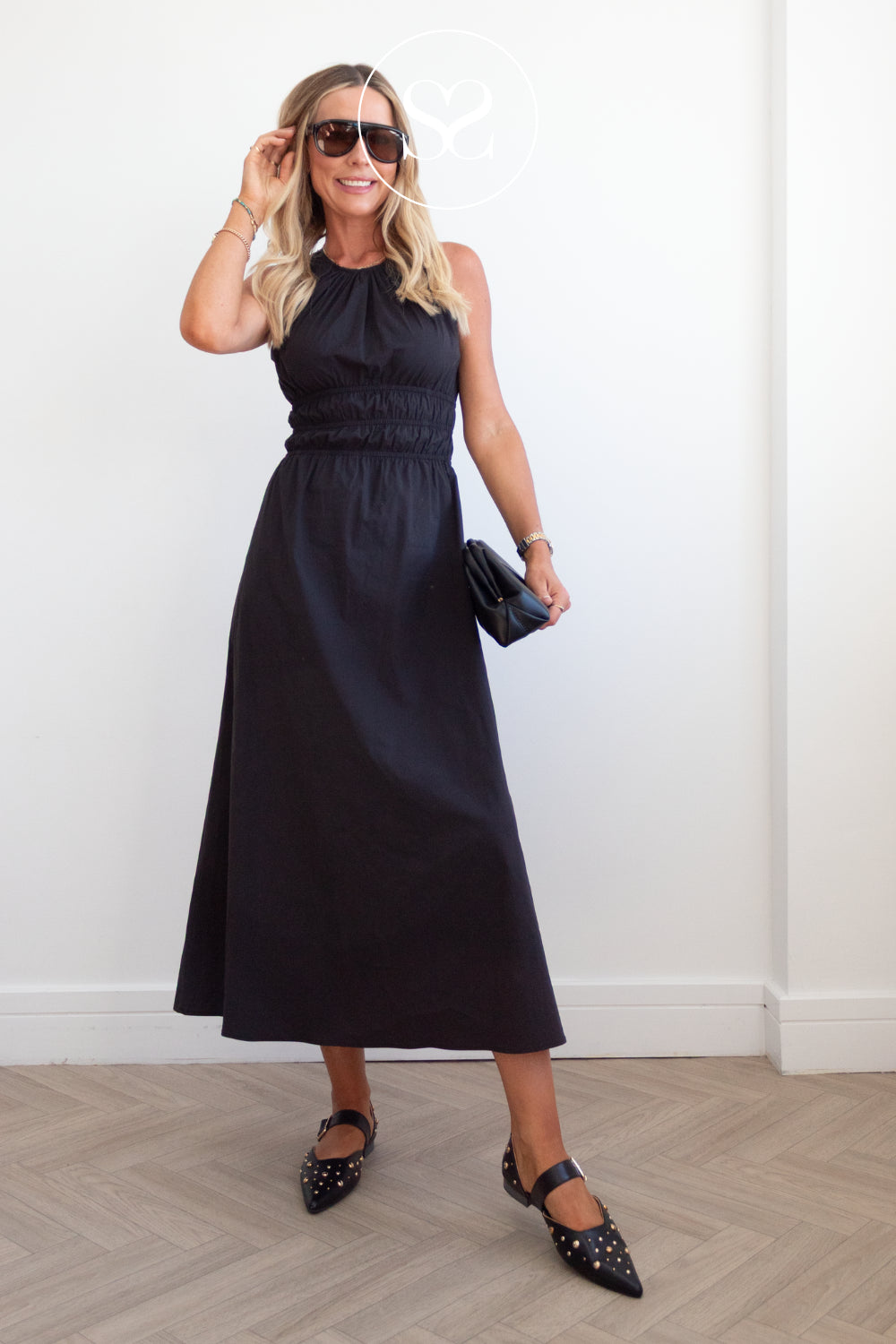 woman wearing black studded mary jane pumps with pointed toe, blakc sunnglasses and black clutch bag