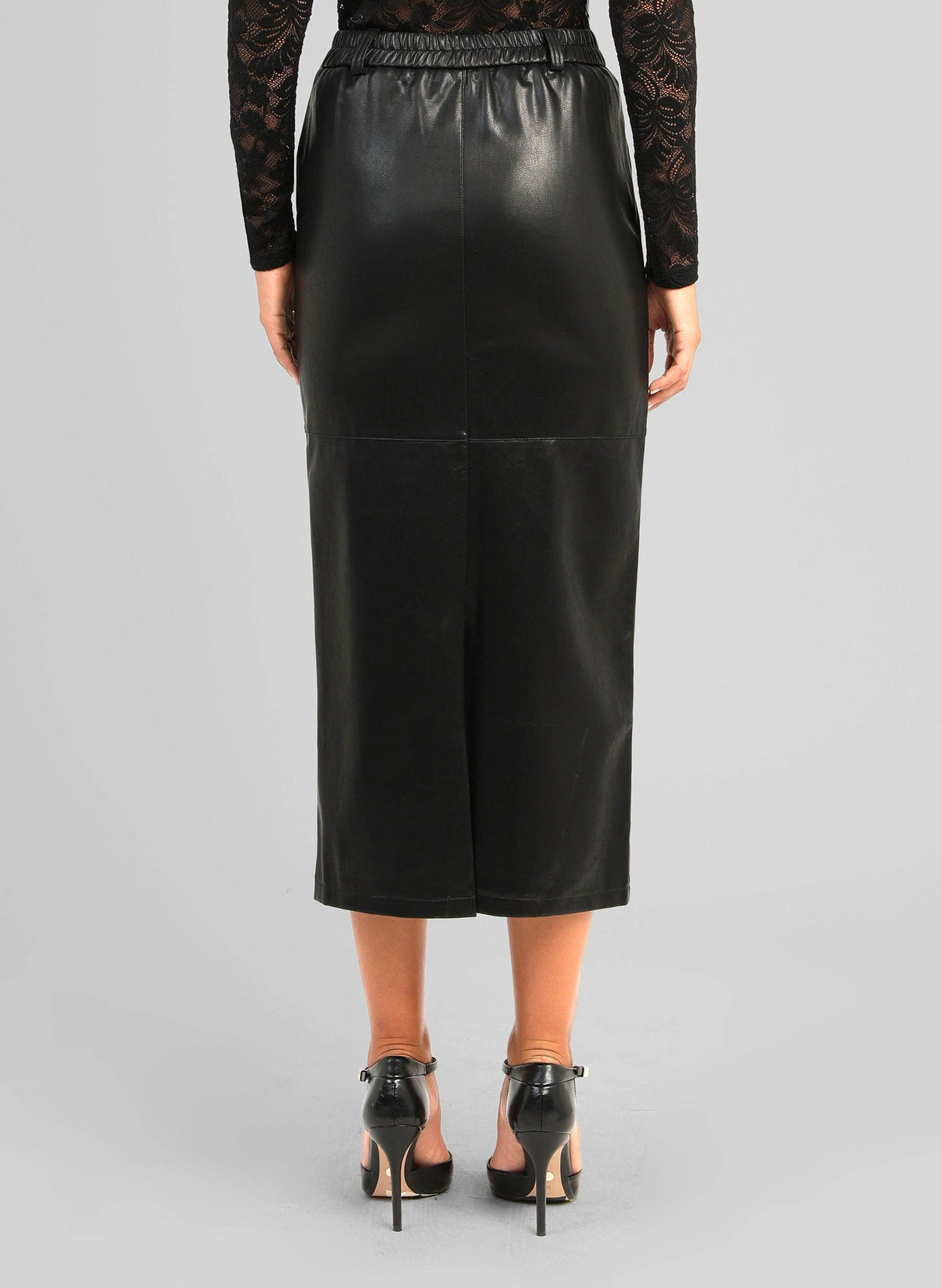A model shown from the back wearing a black faux-leather midi skirt with a smocked waistband, paired with black high heels and a black lace long-sleeve top, against a solid gray studio background.