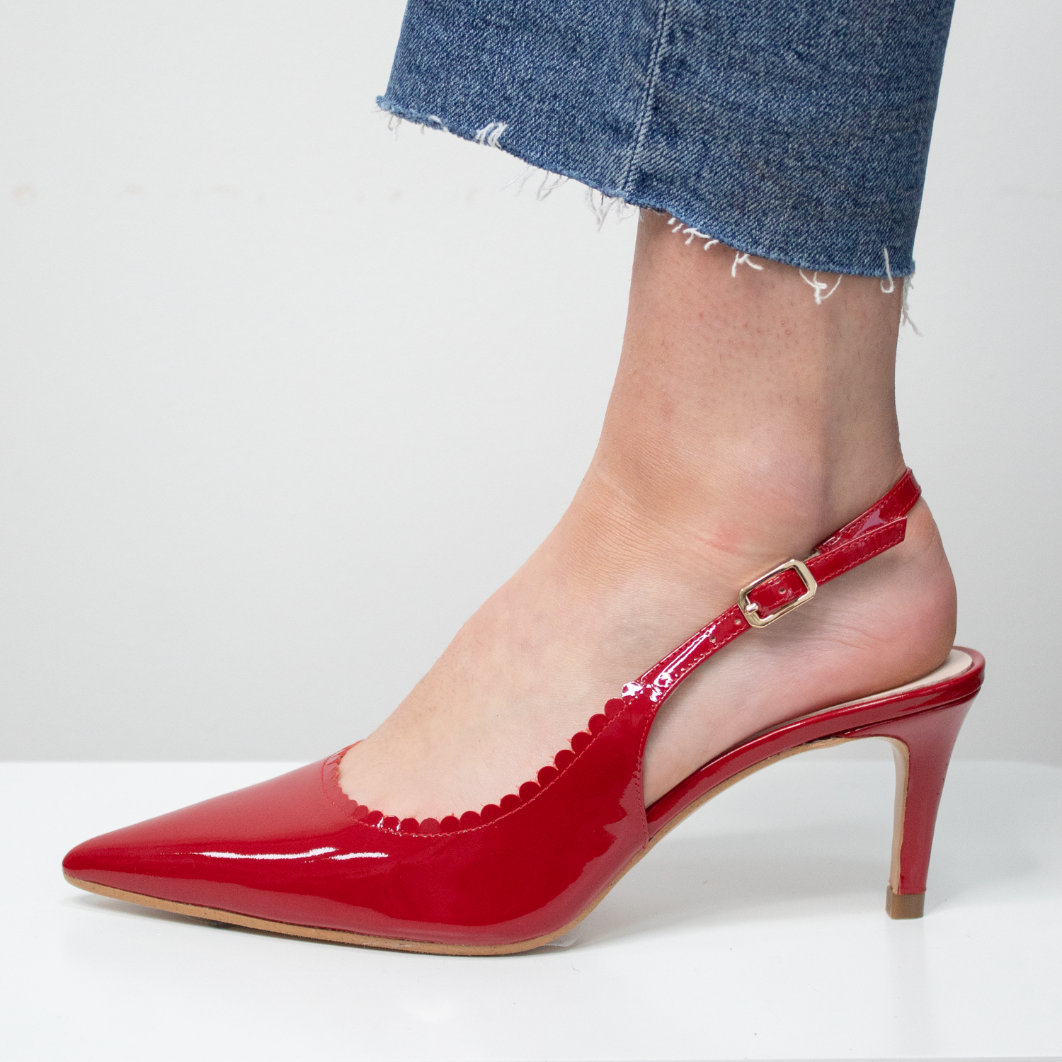 Red patent leather slingback heels / shoes worn with blue jeans on a white background