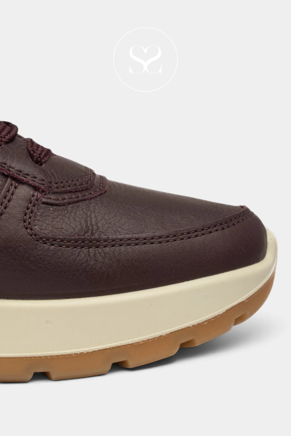 Close-up of a low-top sneaker in dark brown leather with matching brown laces, a thick off-white midsole, and a gum brown outsole, shown on a light gray background.
