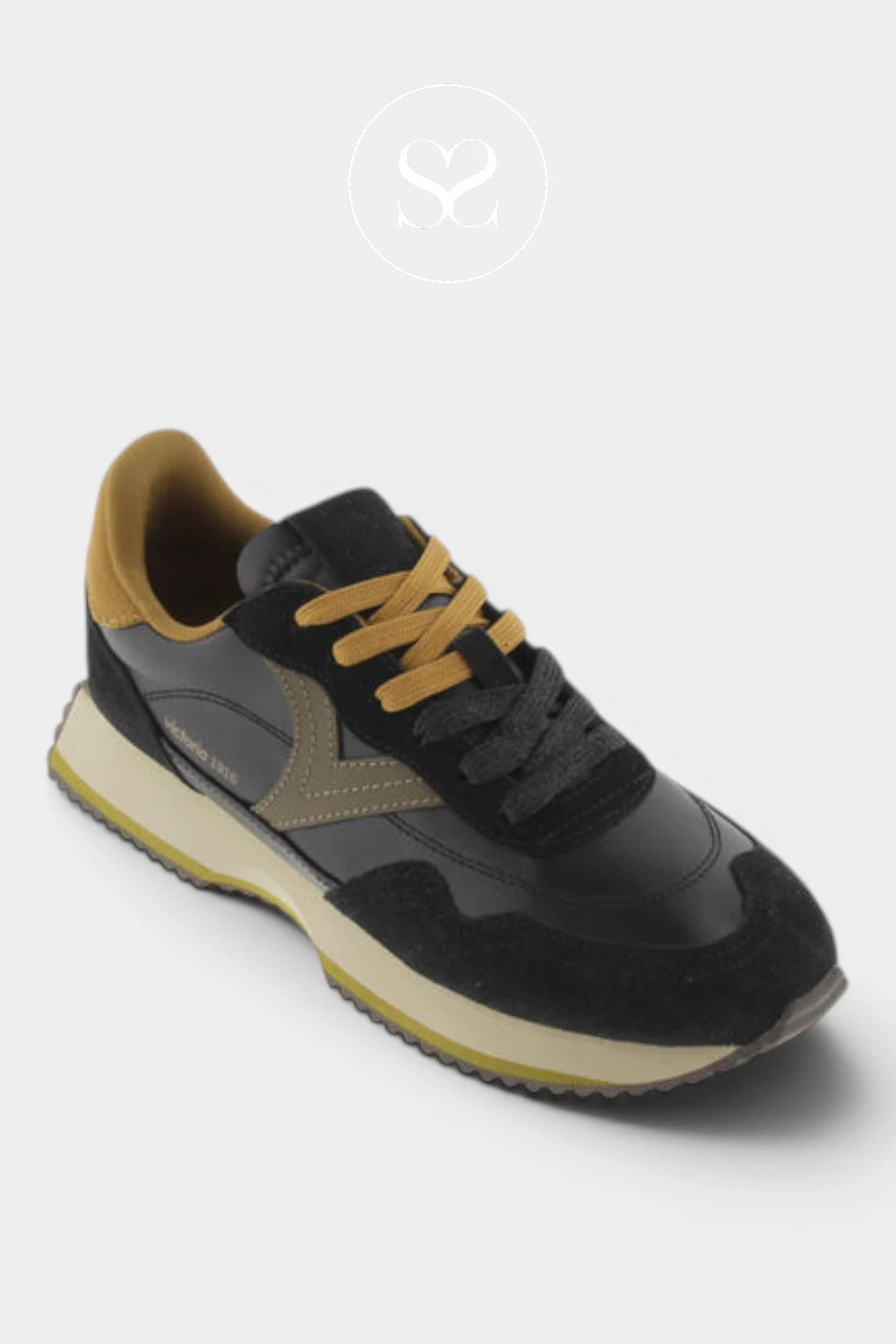 A black and dark gray sneaker with mustard yellow laces, a tan heel tab, and a beige midsole, shown on a light gray background.