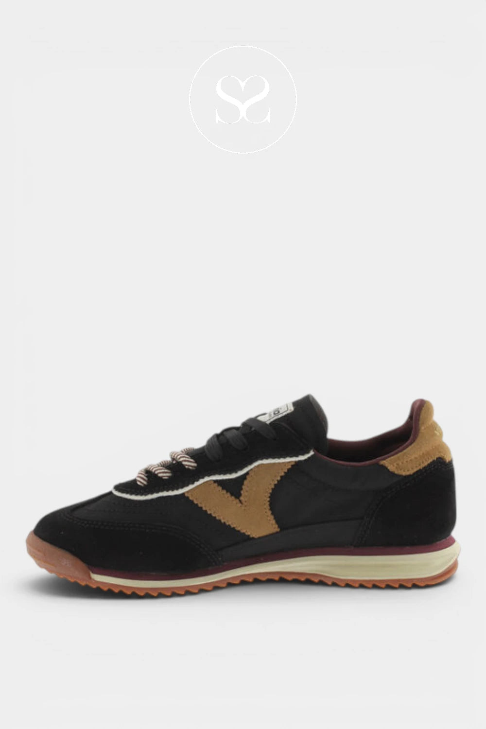 A black low-top sneaker with tan suede overlays, a cream midsole, and a brown gum outsole, shown from a side profile on a light gray background.