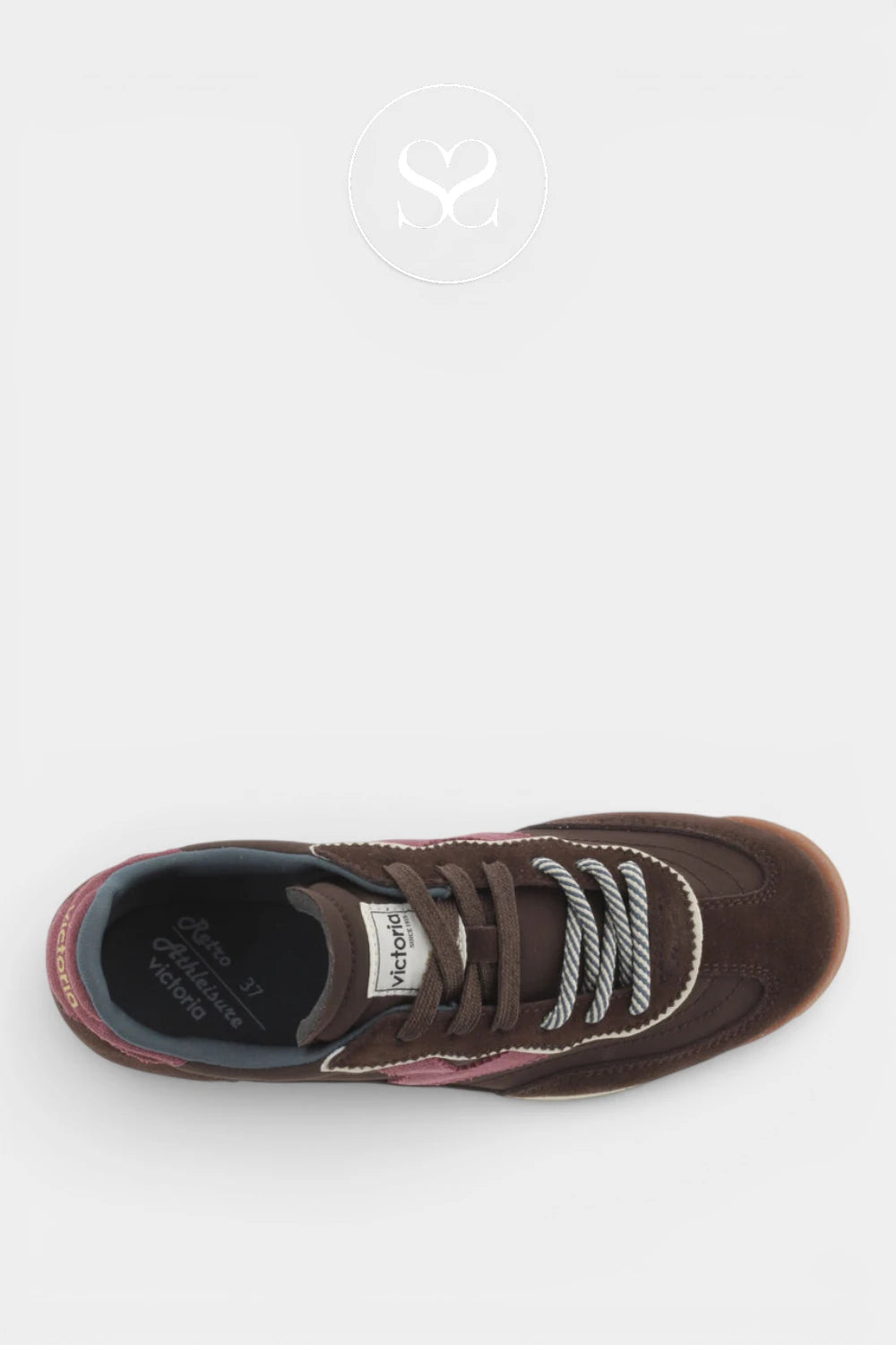 A top-down view of a brown suede sneaker with brown laces, white contrast stitching, and a pink heel tab, set against a light gray background with a faint watermark logo at the top.