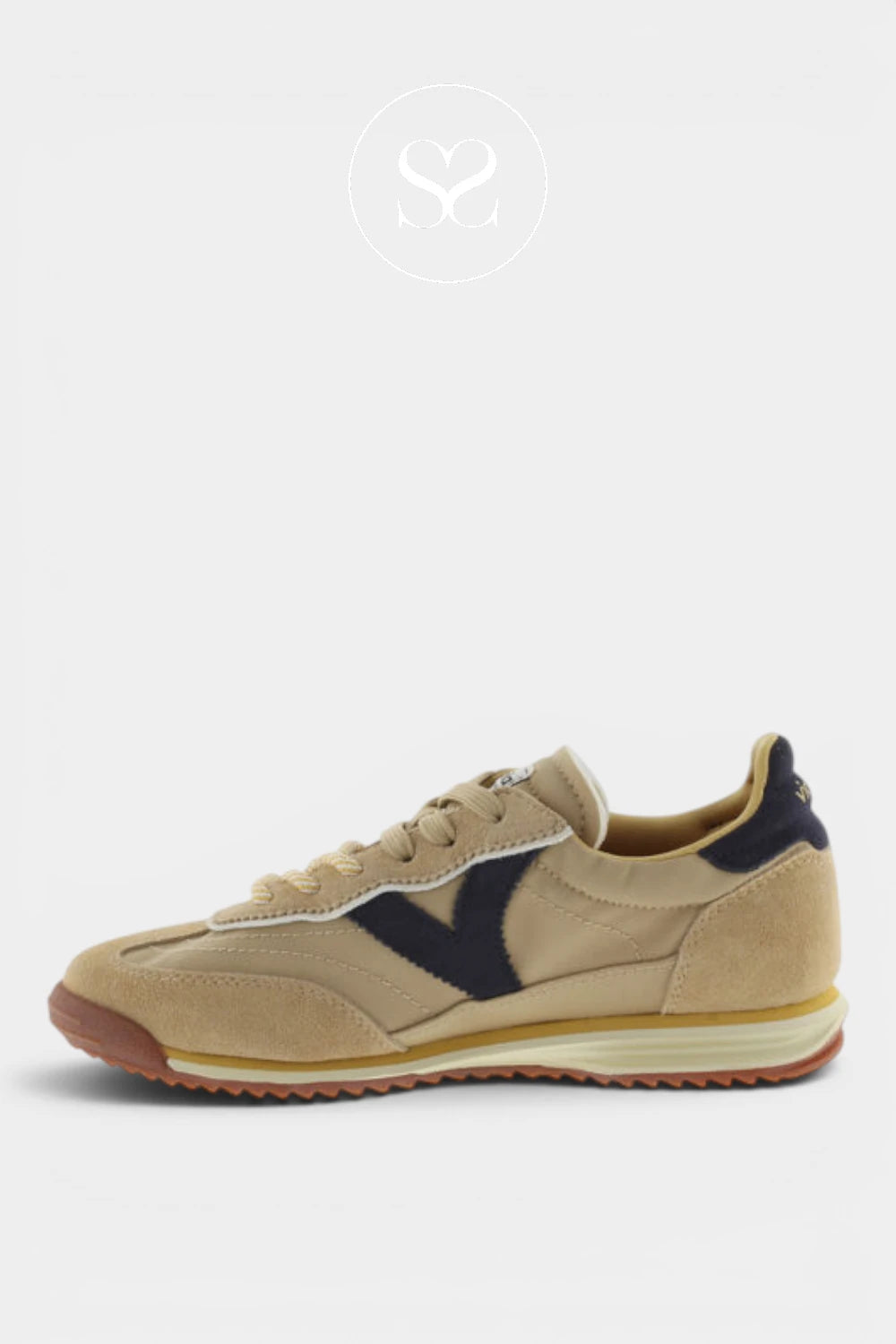 A beige suede sneaker with navy blue side stripes, beige laces, and a brown and cream midsole, shown from the side against a light gray background.