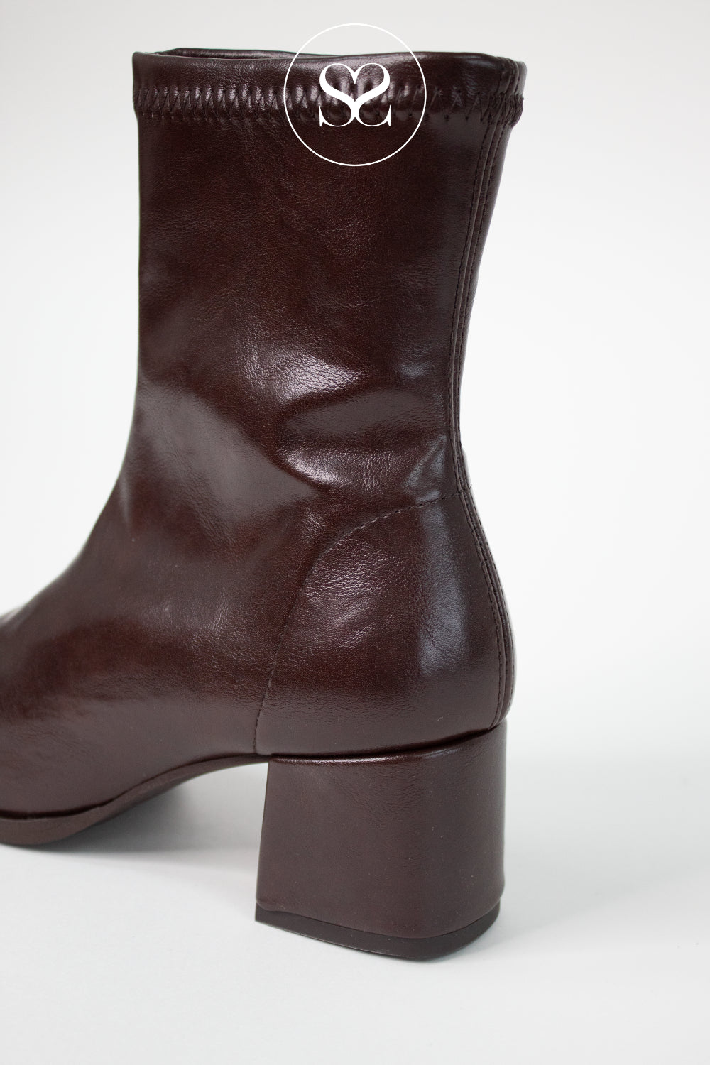 A dark brown leather ankle boot with a block heel, shown from a side-rear angle on a light gray background. A circular logo watermark is visible at the top.