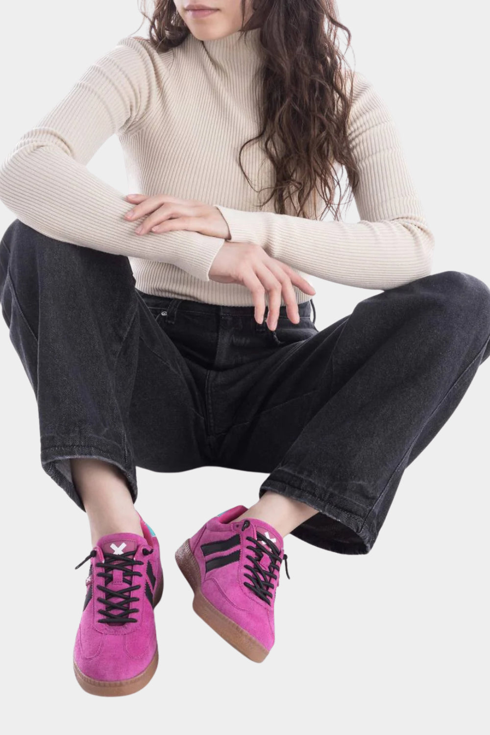 Person wearing a beige sweater and black pants with pink sneakers on a white background