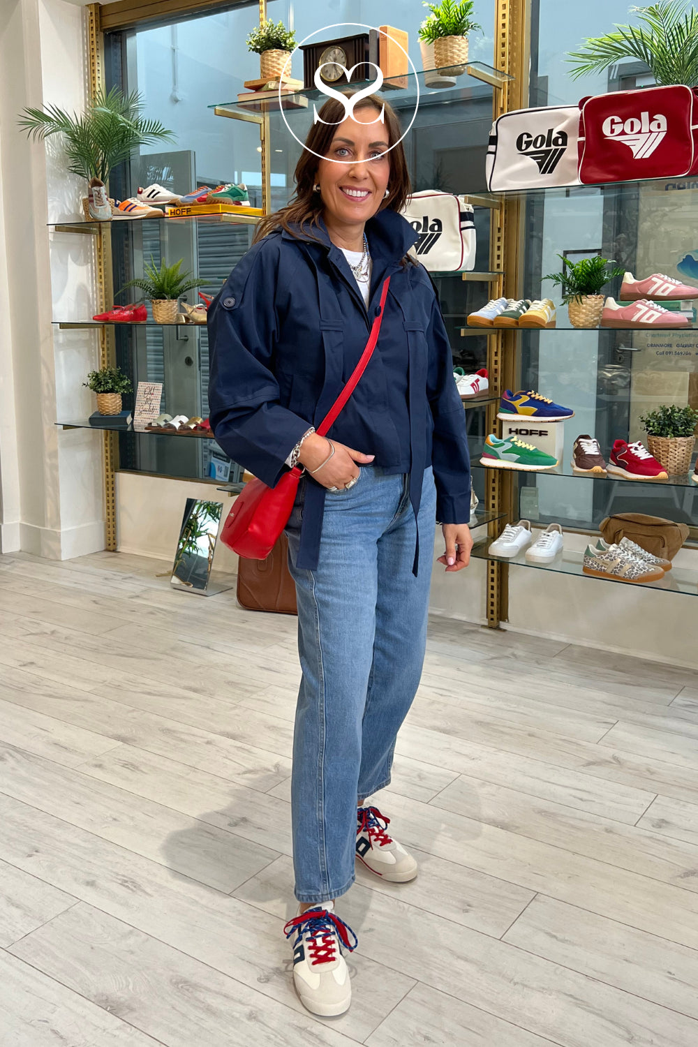 woman wearing white trainers with red & navy double laces paired with red wonders bag and flotte navy rainjacket