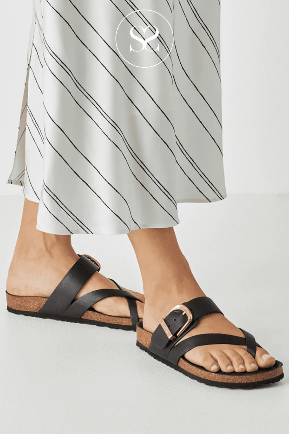 Black sandals worn with white pants on a light gray background