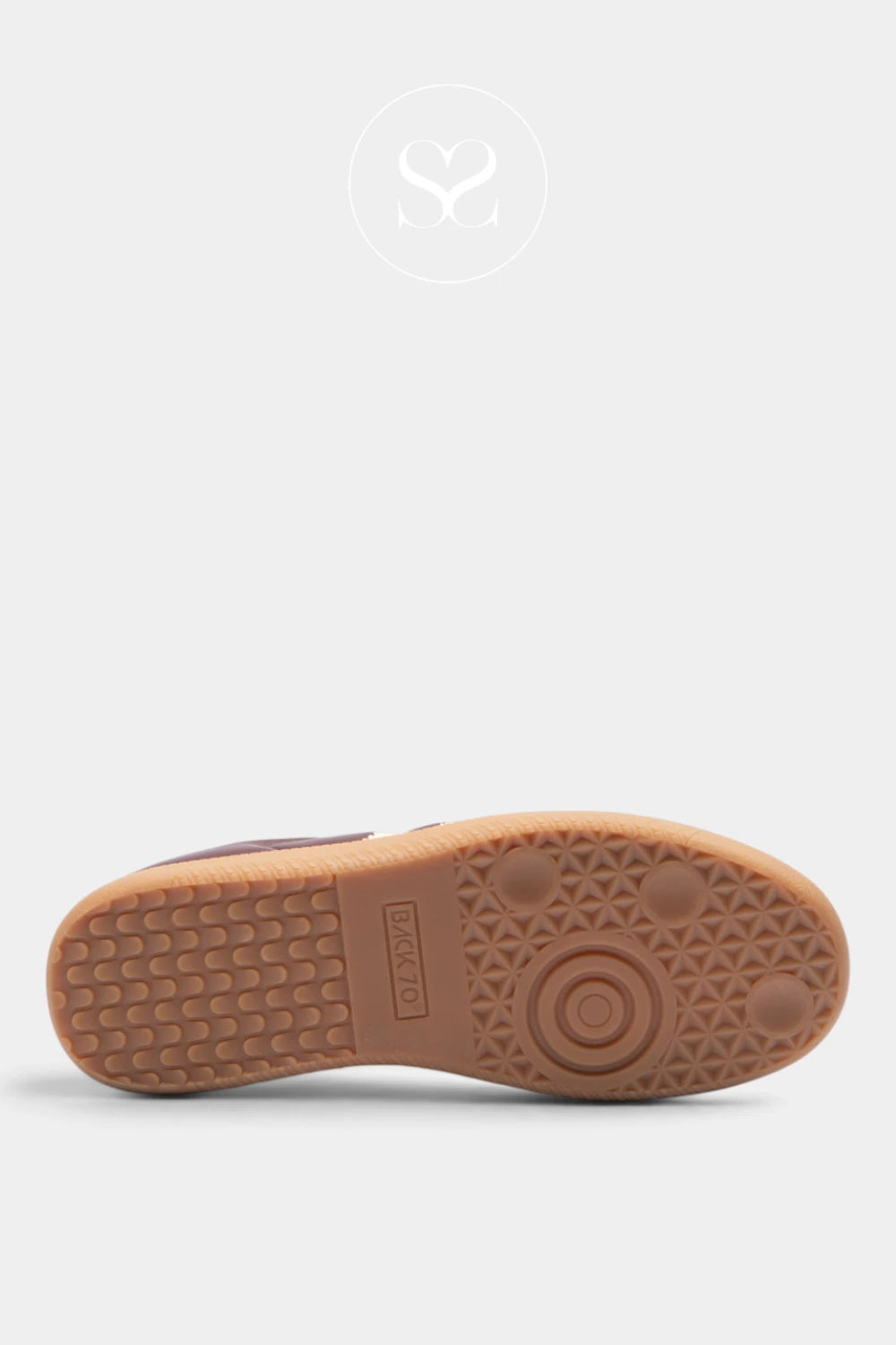 A close-up bottom view of a shoe showing its tan rubber sole with a textured tread pattern and a circular logo embossed in the center, set against a light gray background.