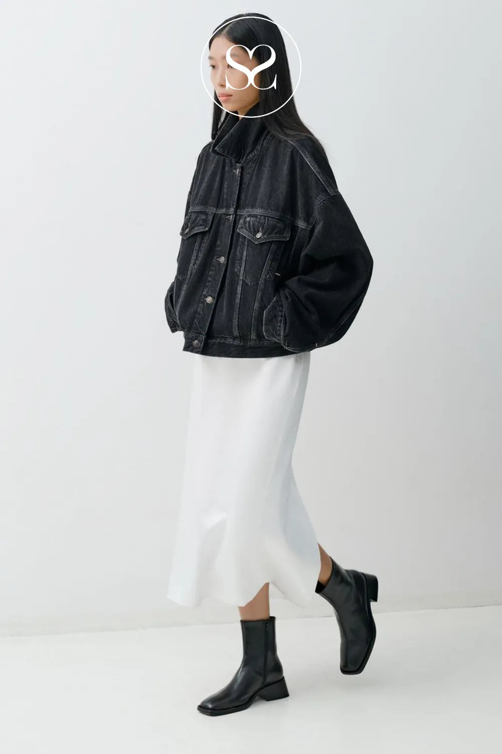 Person wearing a black denim jacket, white pants, and black Vagabond ankle boots on a white background